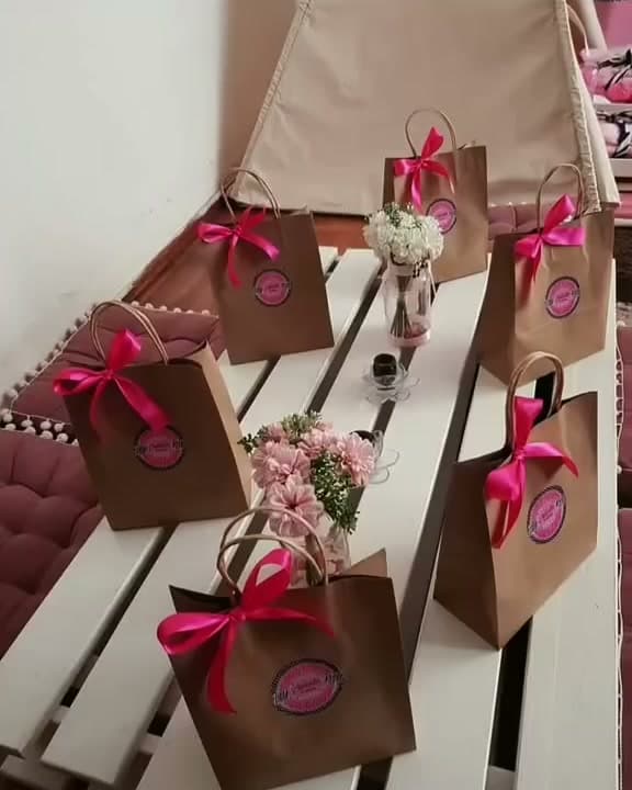 Bolsitas sorpresa de papel kraft con lazos fucsia y logo de Datipi Kids sobre una mesa de pallets blanca con flores